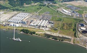 Bird's eye view of an industrial facility on the shore of a large river. Many round and cylindrical tanks in a row. 